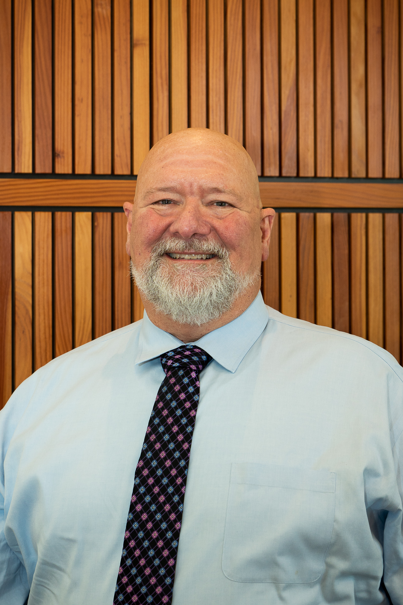 A bald, older White man with a grey beard, smiling.